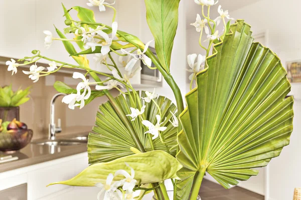 Flowers and green leaves closeup besides kitchen.