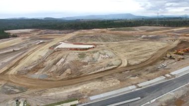 Büyük inşaat alanının gökyüzü panoramik görüntüsü, ağır ekipmanlarla. Arka planda vahşi orman inşaatı var. Drone endüstriyel video.