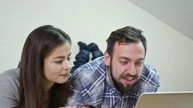 Mutlu çift evde bir yatakta yatarken bir dizüstü bilgisayar kullanarak
