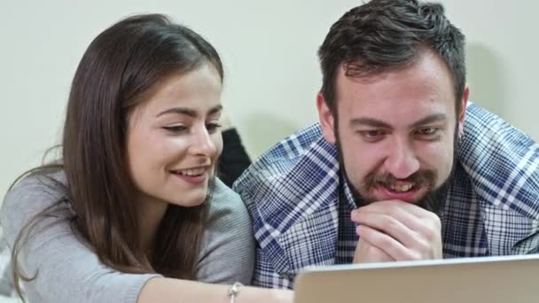 Pareja feliz usando un ordenador portátil acostado en una cama en casa — Vídeos de Stock