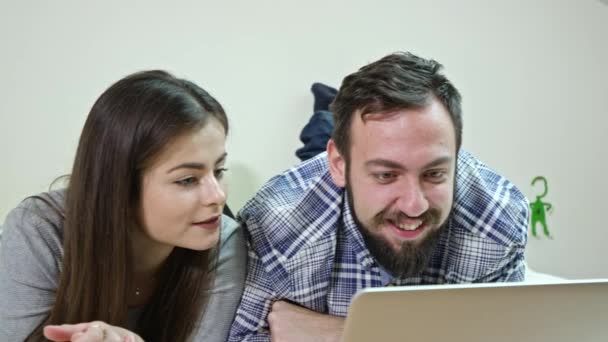 Casal feliz usando um laptop deitado em uma cama em casa — Vídeo de Stock