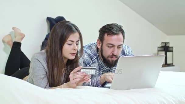 Ευτυχισμένο ζευγάρι χρησιμοποιώντας ένα φορητό υπολογιστή ξαπλωμένος σε ένα κρεβάτι στο σπίτι — Αρχείο Βίντεο