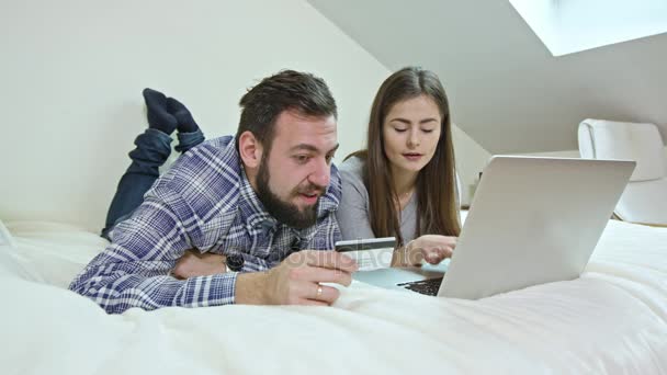 Pareja feliz usando un ordenador portátil acostado en una cama en casa — Vídeo de stock