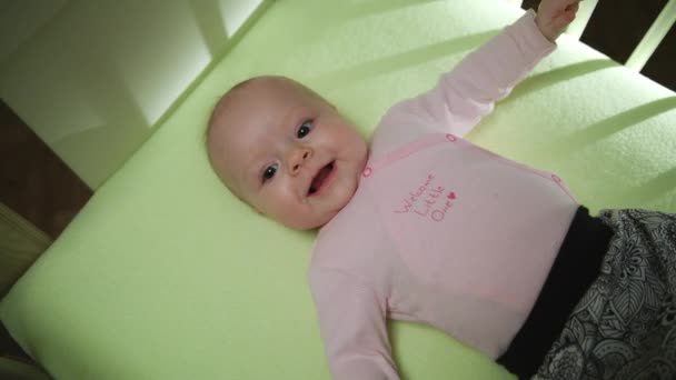 Vista lateral superior del adorable bebé sonriente en tela rosa acostado en la cama y manos y piernas en movimiento — Vídeos de Stock
