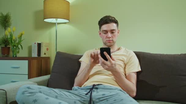 Ο άνθρωπος κάθεται στον καναπέ και χρήση κινητού τηλεφώνου — Αρχείο Βίντεο