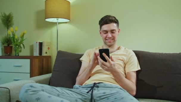 Человек, сидящий на диване и пользующийся мобильным телефоном — стоковое видео
