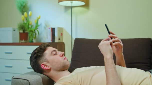 Людина лежить на дивані і використовує мобільний телефон — стокове відео