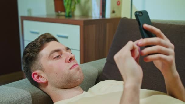 Людина лежить на дивані і використовує мобільний телефон — стокове відео