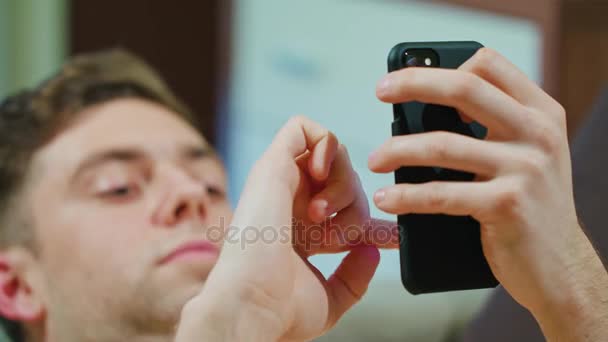 Hombre acostado en el sofá y el uso de teléfono móvil — Vídeos de Stock