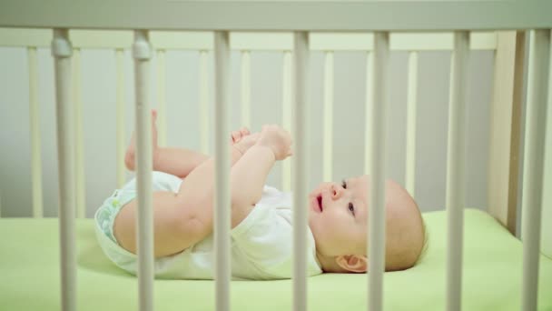 Ребенок, лежащий в детской кроватке дома, ест свои ножки — стоковое видео