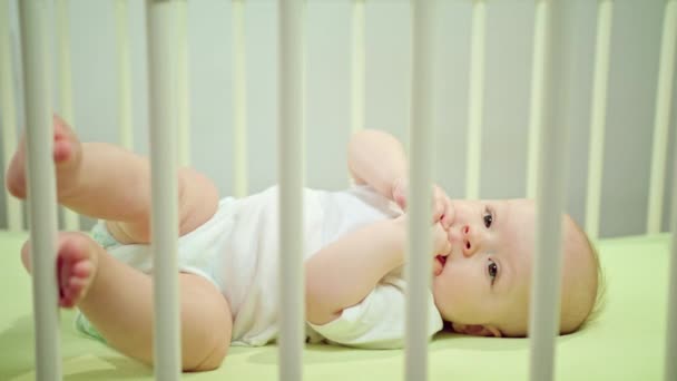 Bebé acostado en una cuna en casa comiendo sus dedos — Vídeos de Stock