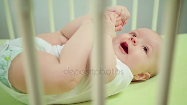 Μωρό ξαπλωμένη σε ένα παχνί που τρώει τα πόδια και τα δάχτυλα — Αρχείο Βίντεο