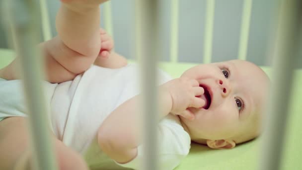 Baby liggend in een kribbe eten zijn vingers — Stockvideo