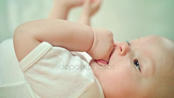 Bebé acostado en la cama en casa comiendo su dedo — Vídeos de Stock
