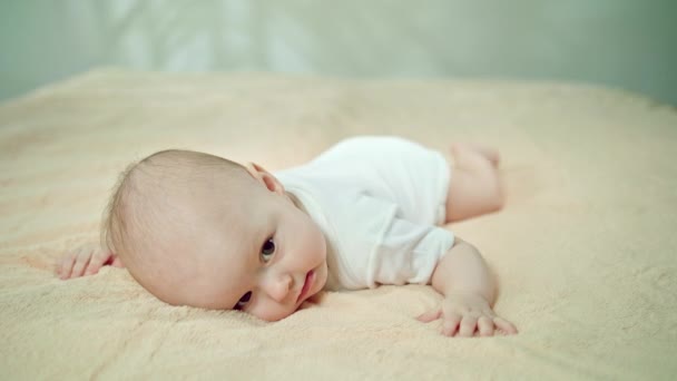 Bebé acostado boca abajo sobre una suave ropa de cama sonriendo — Vídeos de Stock