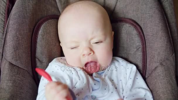 Lindo bebé acostado en Pram comiendo una cuchara roja — Vídeos de Stock