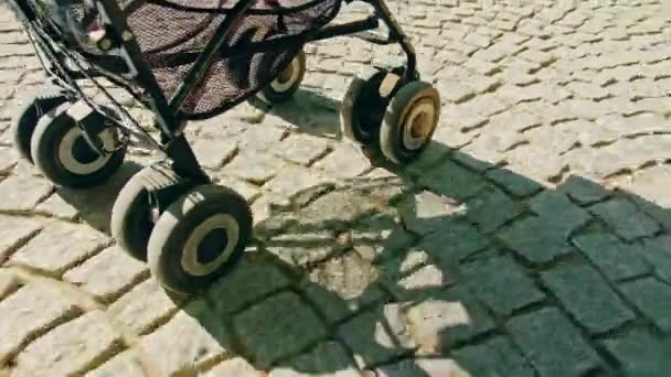 Arnavut kaldırımı taşı yolda inişli çıkışlı bir bebek arabası ve tekerlekli — Stok video