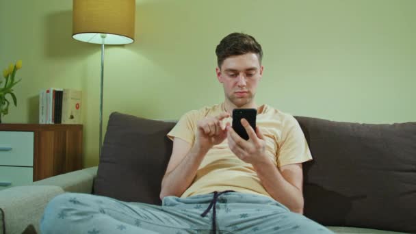 Człowiek siedzi na kanapie i przy użyciu telefonu komórkowego — Wideo stockowe