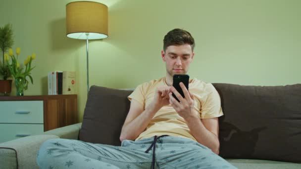 Mann sitzt auf dem Sofa und benutzt Handy — Stockvideo