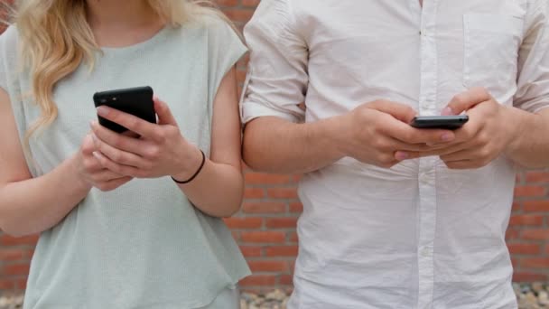 Un jeune couple utilisant des téléphones mobiles à l'extérieur — Video