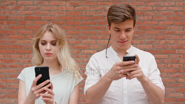 Una joven pareja usando teléfonos móviles al aire libre — Vídeo de stock