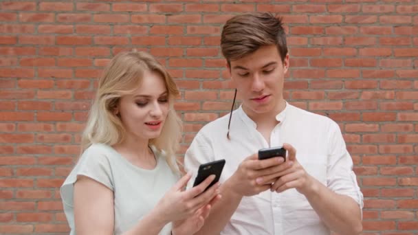 Una joven pareja usando teléfonos móviles al aire libre — Vídeo de stock