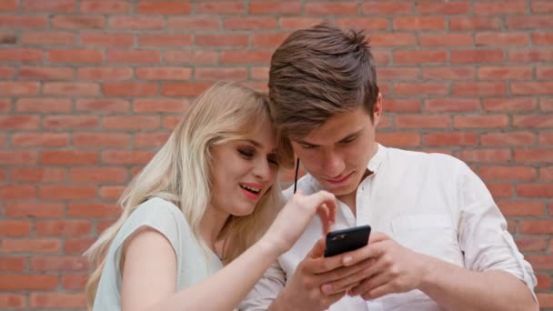 Una joven pareja usando un teléfono móvil al aire libre — Vídeo de stock