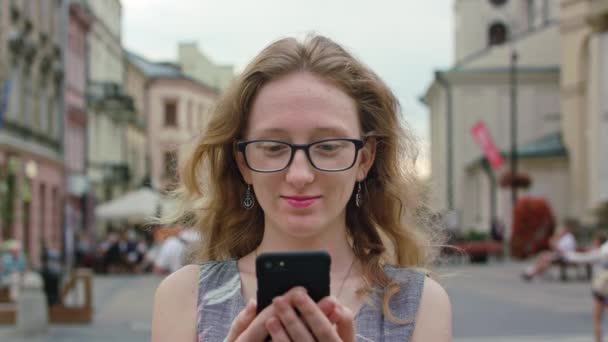 Ein schöner Rotschopf mit einem Handy im Freien — Stockvideo