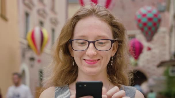 Egy gyönyörű vörös hajú, használ egy mozgatható telefon a szabadban — Stock videók