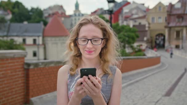 Una hermosa pelirroja usando un teléfono móvil al aire libre — Vídeos de Stock