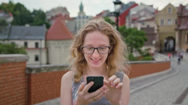 Una hermosa pelirroja usando un teléfono móvil al aire libre — Vídeos de Stock