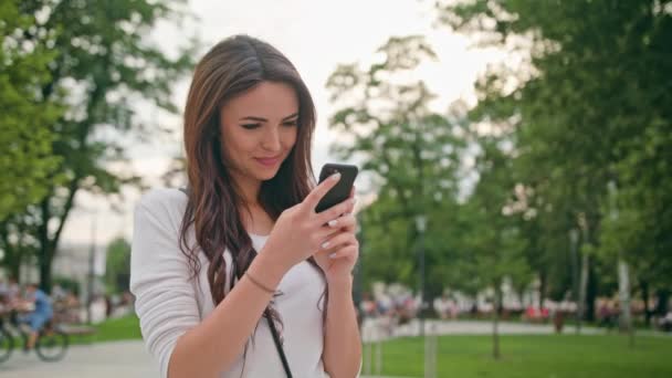 Piękna Brunetka, przy użyciu telefonu komórkowego na świeżym powietrzu — Wideo stockowe