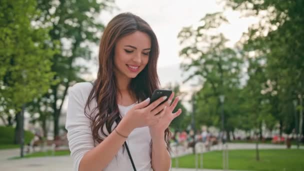 Piękna Brunetka, przy użyciu telefonu komórkowego na świeżym powietrzu — Wideo stockowe