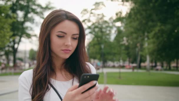 En vacker brunett med en mobiltelefon-utomhus — Stockvideo