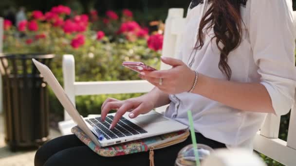 Señora sentada en el parque y el uso de ordenador portátil y teléfono — Vídeos de Stock