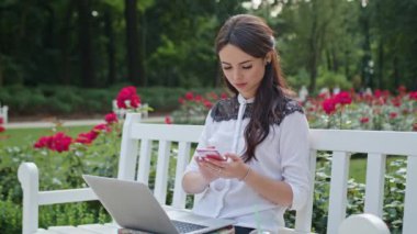 Bayan parkta oturan ve Laptop ve telefon kullanma