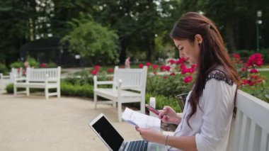 Bayan parkta oturan ve Laptop ve telefon kullanma