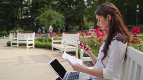 여자는 공원에 앉아서 노트북 및 휴대 전화를 사용 하 여 — 비디오