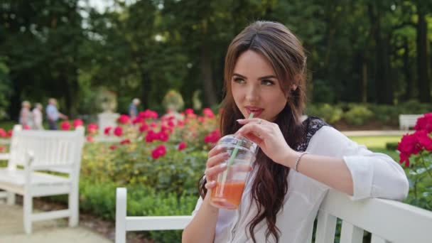 Brunnette Lady Sitting on a Bench in the Park Drinking — Stock Video