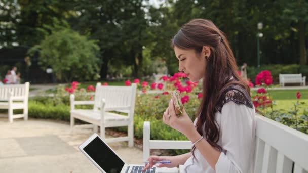 Señora sentada en el banco en el parque y el uso de ordenador portátil — Vídeos de Stock