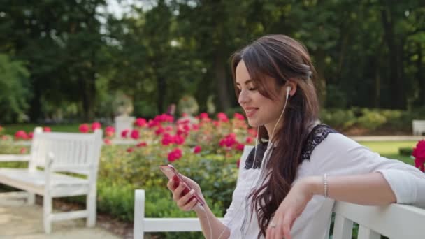 Леді в парку, прослуховування музики на телефон — стокове відео