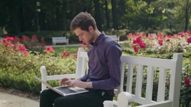 Yorgun genç adam parkta bir dizüstü bilgisayar kullanarak