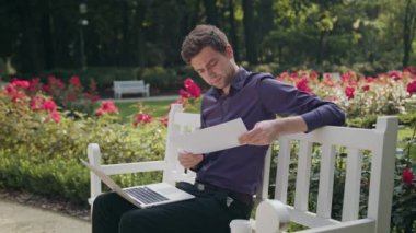 Bir dizüstü bilgisayar ve kağıt kullanarak parkta genç adam
