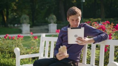 Genç adam parkta Tablet kullanma ve yeme