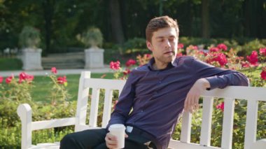 Genç adam parkta bir kahve içer