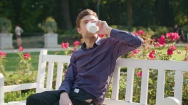 Genç adam parkta bir kahve içer