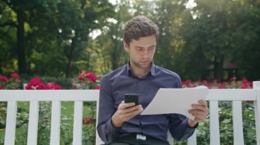 Genç adam parkta bir telefonu kullanarak ve okuma