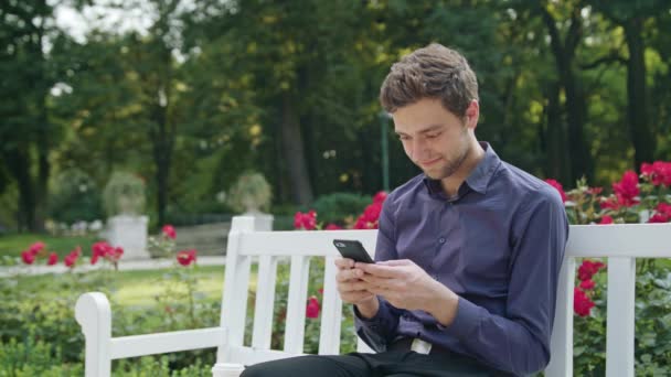 A fiatalember a parkban segítségével a telefon — Stock videók