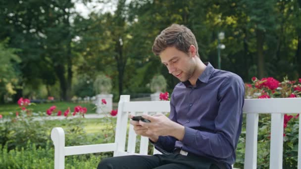 Молодой человек в парке с помощью телефона играет в игры — стоковое видео