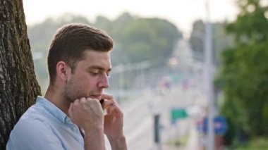 Bir ağacın altında telefonda konuşan bir genç adam